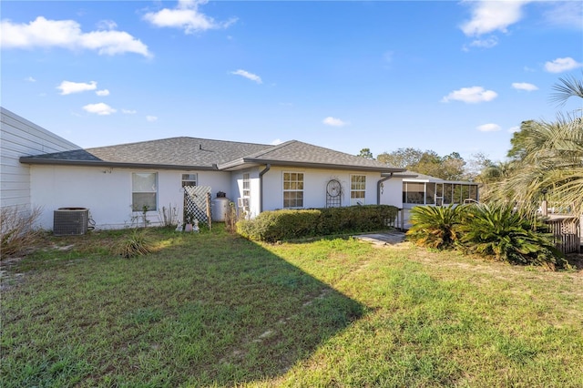 back of property featuring roof with shingles, a sunroom, stucco siding, central air condition unit, and a lawn