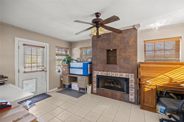 interior space with a tiled fireplace, ornamental molding, light tile patterned flooring, a textured ceiling, and a ceiling fan