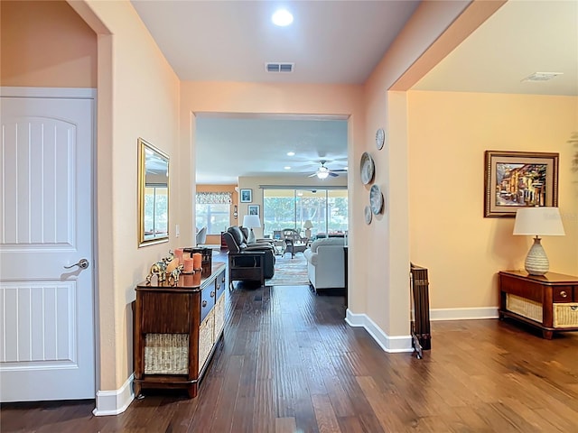 hallway with dark wood finished floors, visible vents, and baseboards