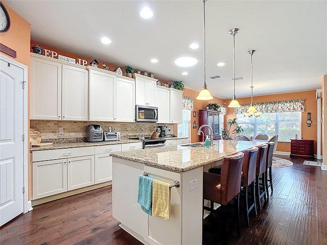 kitchen with tasteful backsplash, a center island with sink, dark wood-style floors, stainless steel appliances, and a sink