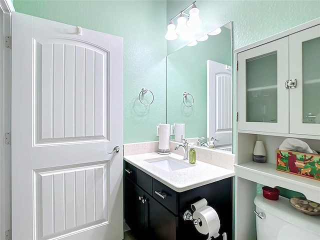 half bath featuring vanity, toilet, and a textured wall