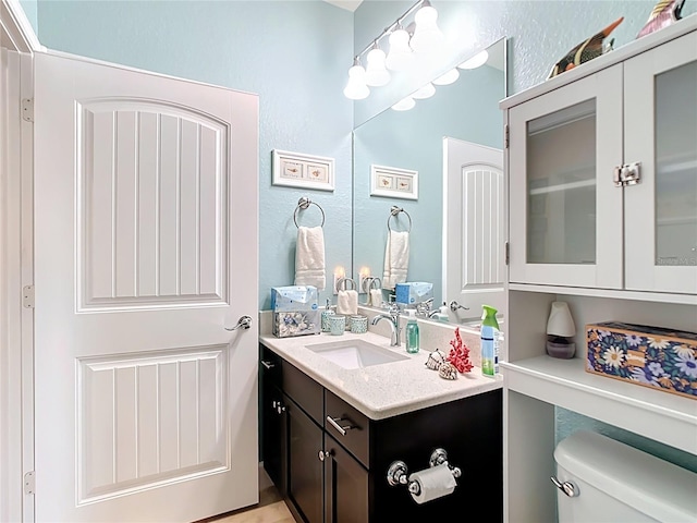 half bath with toilet, vanity, and a textured wall