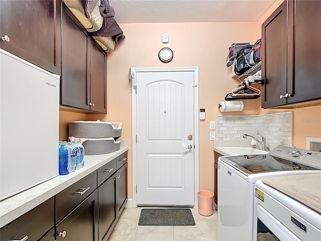 laundry room featuring a sink, light tile patterned floors, cabinet space, a textured ceiling, and separate washer and dryer