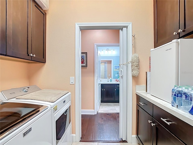 laundry area with baseboards, washing machine and clothes dryer, light wood-style flooring, cabinet space, and a sink