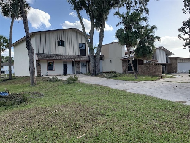 view of front of property featuring board and batten siding, concrete driveway, and a front lawn