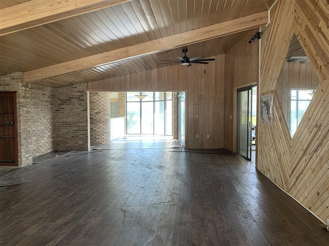 unfurnished living room with a wealth of natural light, wooden walls, vaulted ceiling with beams, and wood-type flooring