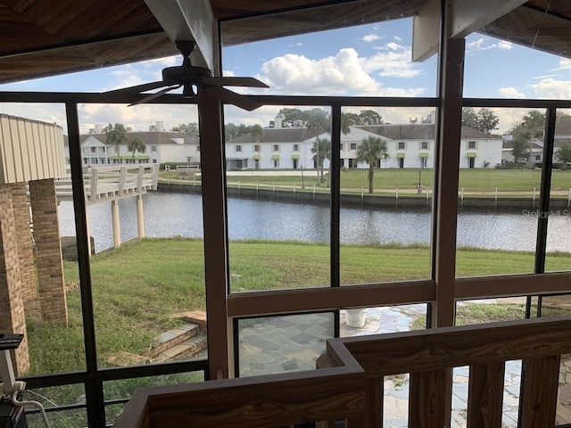 unfurnished sunroom with a residential view, a ceiling fan, and a water view