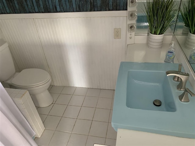 half bathroom featuring tile patterned floors, a wainscoted wall, toilet, and a sink