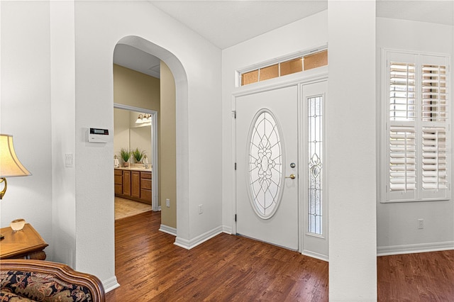 foyer entrance with baseboards, arched walkways, and wood finished floors