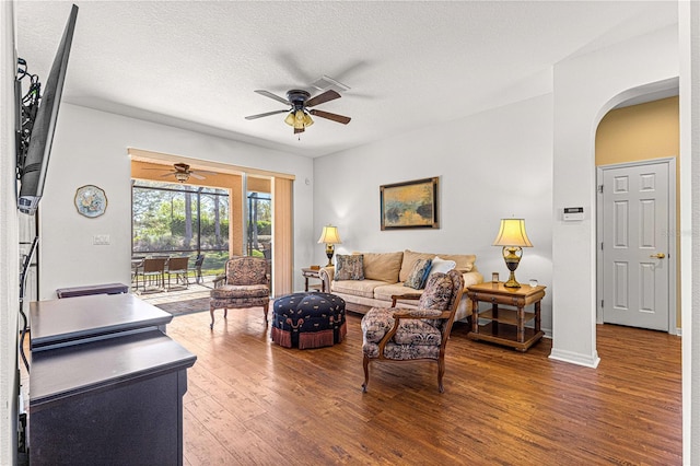 living area featuring a ceiling fan, a textured ceiling, wood finished floors, arched walkways, and baseboards