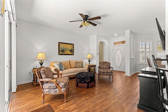 living area featuring arched walkways, baseboards, ceiling fan, and wood finished floors