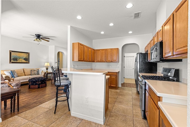 kitchen with visible vents, arched walkways, stainless steel appliances, a kitchen breakfast bar, and open floor plan