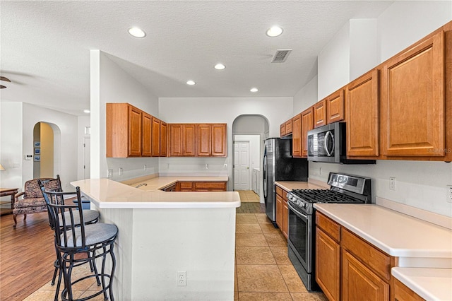 kitchen with visible vents, arched walkways, a peninsula, appliances with stainless steel finishes, and a breakfast bar area