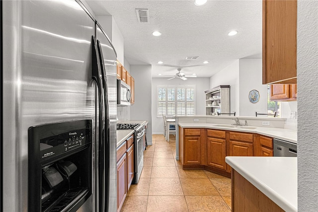 kitchen featuring brown cabinets, a ceiling fan, a sink, appliances with stainless steel finishes, and a peninsula