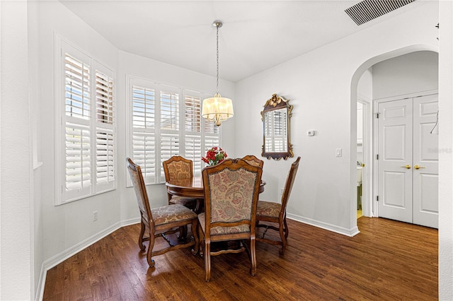 dining room featuring arched walkways, a notable chandelier, a healthy amount of sunlight, and wood finished floors