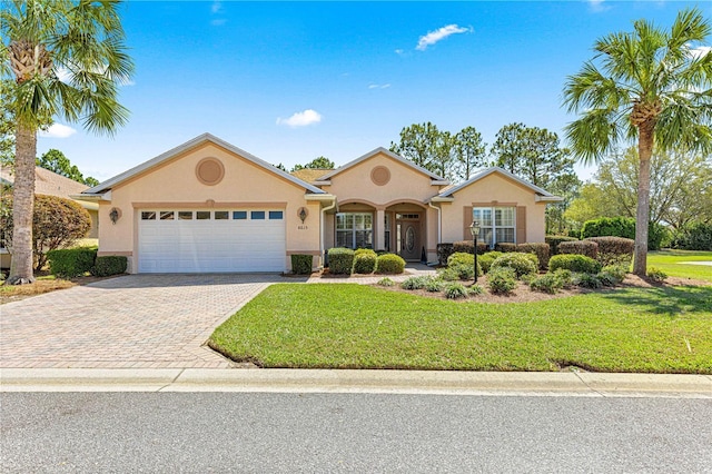 view of front of house featuring stucco siding, decorative driveway, a garage, and a front lawn