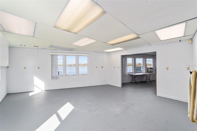 spare room featuring a drop ceiling, baseboards, and concrete flooring