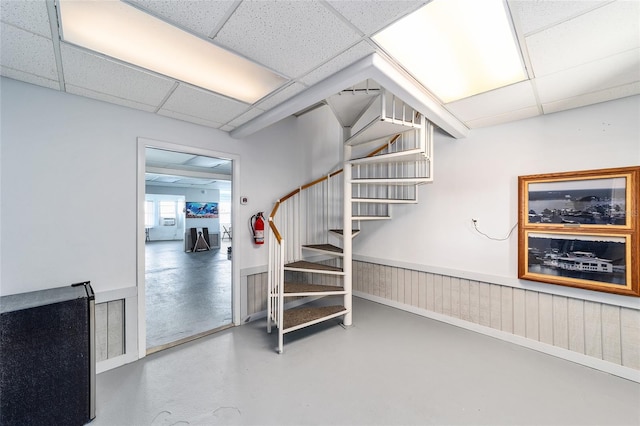 staircase with a drop ceiling, concrete flooring, and wainscoting