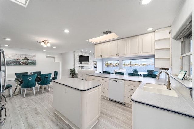 kitchen featuring dishwasher, a kitchen island, white cabinetry, and a sink