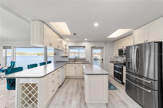 kitchen featuring a kitchen island, decorative backsplash, a peninsula, stainless steel appliances, and a sink