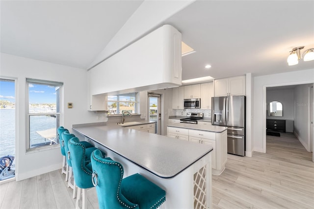 kitchen featuring a sink, stainless steel appliances, a peninsula, light wood finished floors, and decorative backsplash