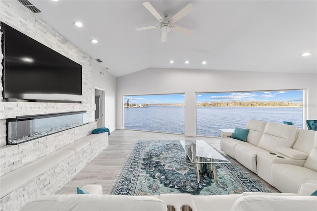 living area with visible vents, ceiling fan, vaulted ceiling, a stone fireplace, and wood finished floors