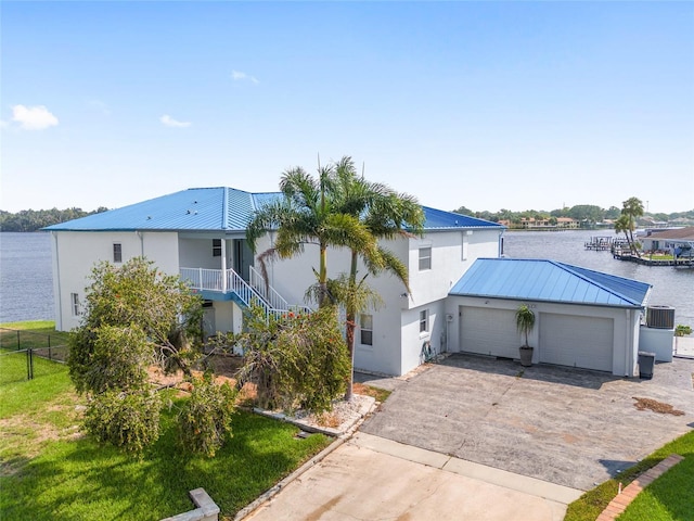 exterior space featuring a water view, concrete driveway, stairs, metal roof, and an attached garage