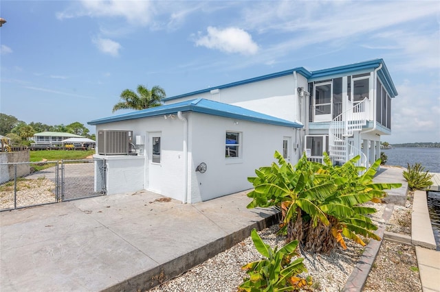 view of side of home with central air condition unit, stucco siding, a sunroom, a patio, and a gate