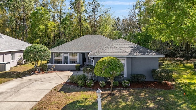 single story home featuring roof with shingles, a front yard, driveway, and stucco siding