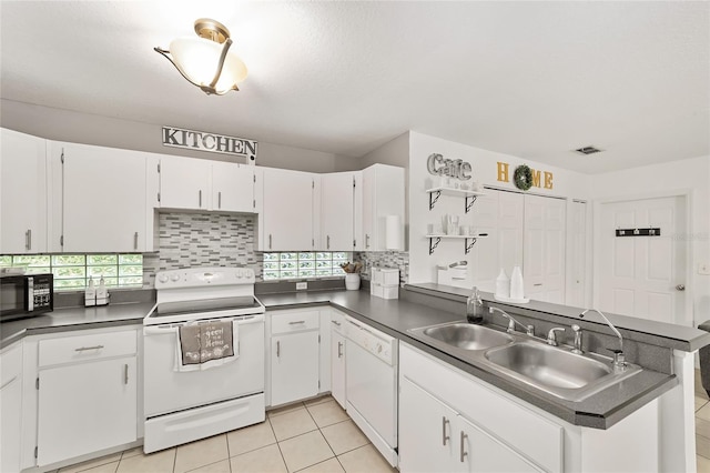 kitchen with dark countertops, decorative backsplash, a peninsula, white appliances, and a sink