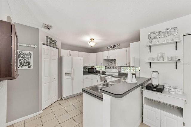 kitchen with dark countertops, backsplash, a peninsula, light tile patterned flooring, and white appliances