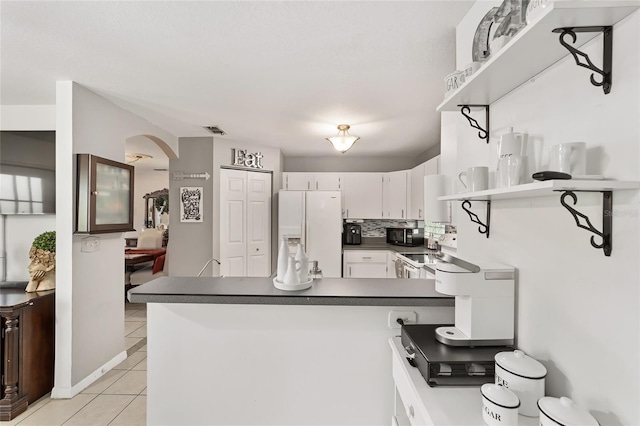 kitchen featuring visible vents, dark countertops, white appliances, a peninsula, and light tile patterned floors