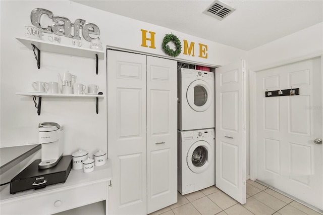 clothes washing area featuring laundry area, stacked washer / dryer, light tile patterned floors, and visible vents