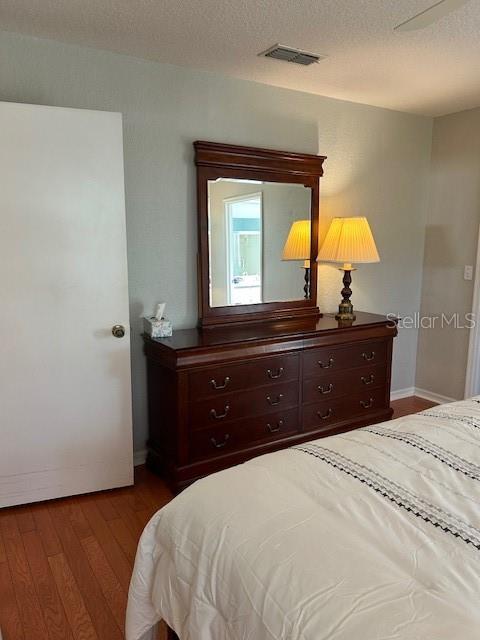 bedroom featuring visible vents, baseboards, a textured ceiling, and dark wood finished floors