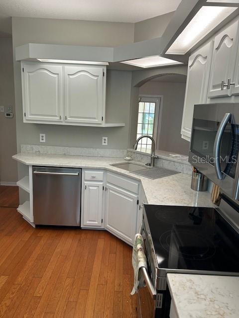 kitchen with a sink, arched walkways, light wood-style floors, and stainless steel appliances