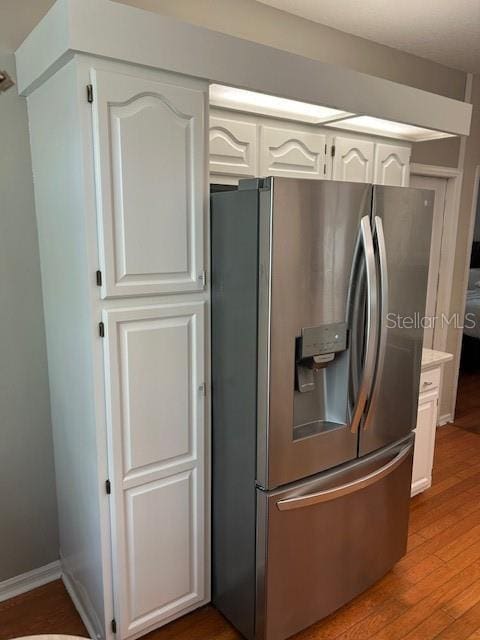 kitchen featuring baseboards, stainless steel fridge, light countertops, white cabinetry, and wood finished floors