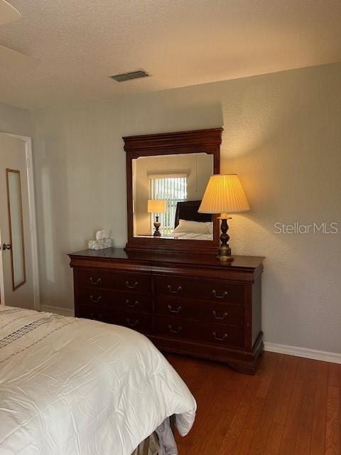 bedroom with visible vents, baseboards, a textured ceiling, and dark wood-style floors