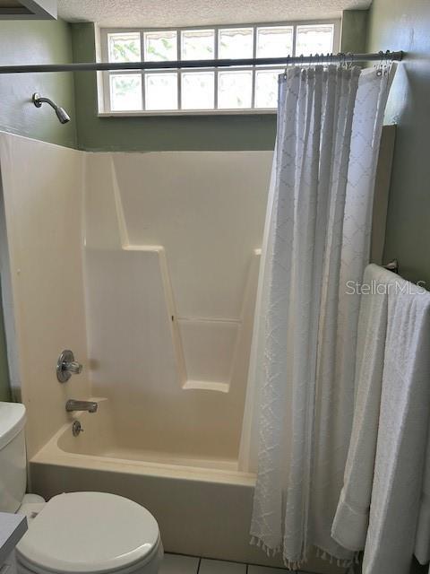 bathroom with tile patterned floors, shower / bath combo with shower curtain, and toilet