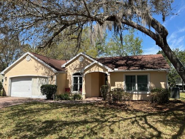 ranch-style house featuring an attached garage, driveway, stucco siding, and a front yard