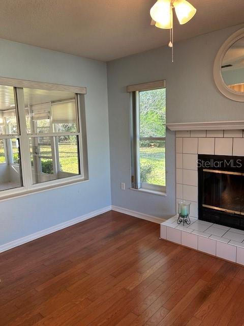 unfurnished living room featuring ceiling fan, wood finished floors, a fireplace, and baseboards
