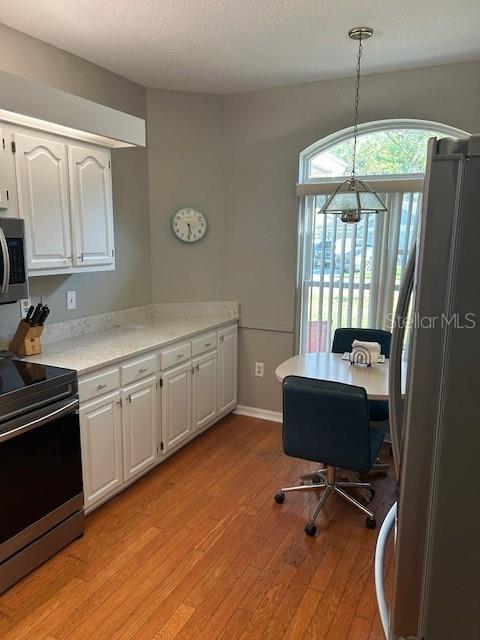 interior space featuring light wood-type flooring, white cabinetry, light countertops, stainless steel appliances, and hanging light fixtures