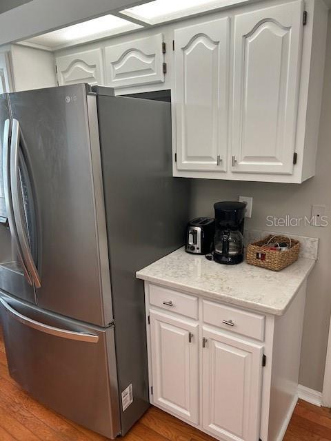 kitchen featuring white cabinets, stainless steel fridge, wood finished floors, and baseboards