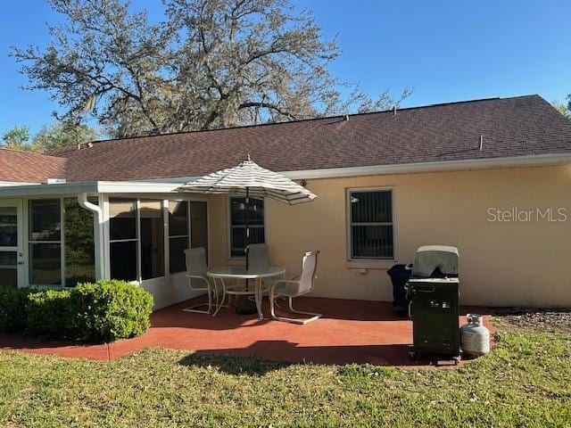 back of house with a sunroom, a lawn, a patio, stucco siding, and roof with shingles