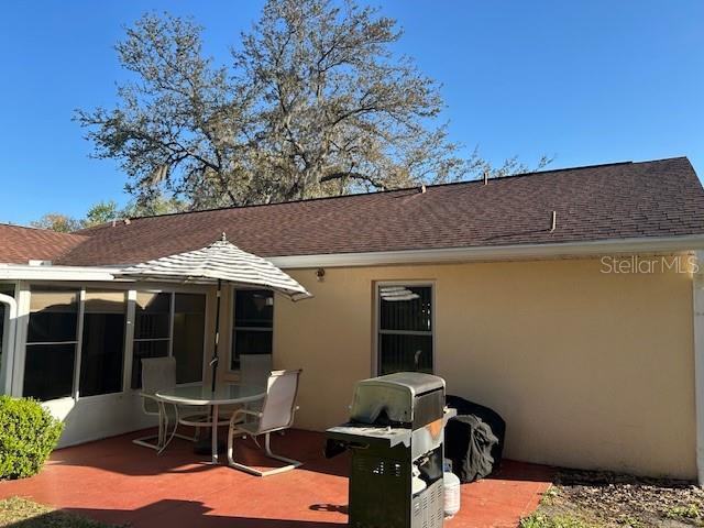 back of house with a shingled roof, a patio, and stucco siding