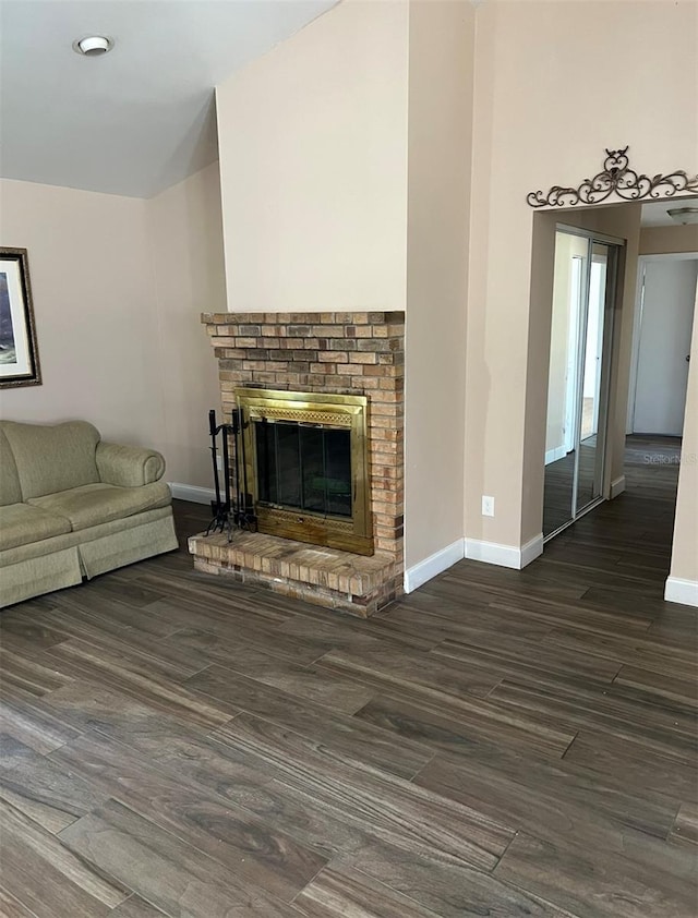 unfurnished living room with baseboards, a brick fireplace, wood finished floors, and a towering ceiling