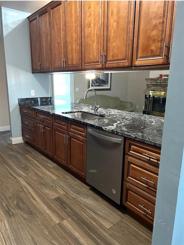 kitchen featuring baseboards, dishwasher, dark stone counters, a stone fireplace, and a sink