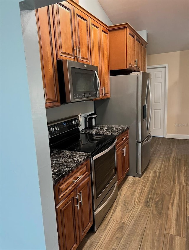 kitchen featuring dark stone countertops, stainless steel appliances, brown cabinets, and dark wood finished floors