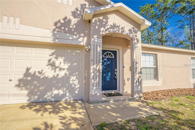 view of exterior entry with stucco siding, a garage, and concrete driveway