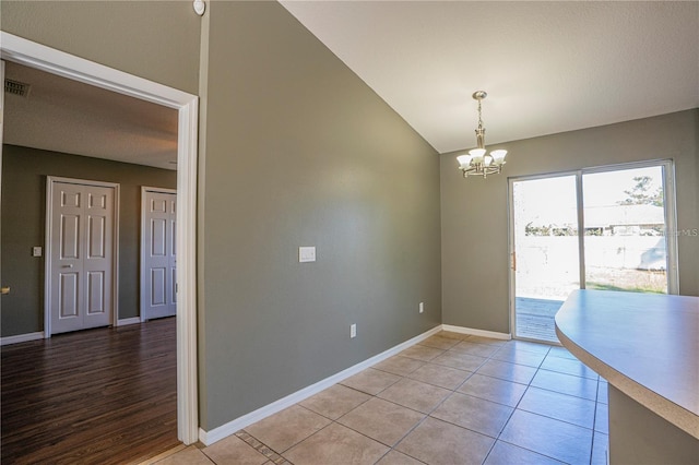 empty room with visible vents, a notable chandelier, lofted ceiling, light tile patterned floors, and baseboards