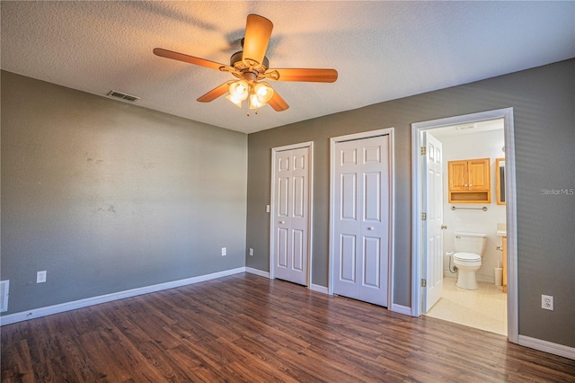 unfurnished bedroom featuring visible vents, multiple closets, a textured ceiling, wood finished floors, and baseboards
